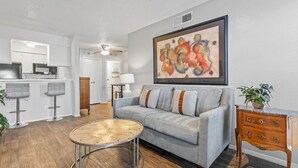 Uma sala de estar moderna com um sofá cinzento, uma mesa de centro redonda e um quadro na parede.
