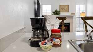 A kitchen counter with a coffee maker, a jar of Great Value Classic Roast Tostado, a bowl of yogurt, and a napkin dispenser. - Cute & Contemporary 1 Bed Apt! Easy Pool Access! (Dallas)