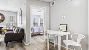 Een moderne woonkamer met een bank, een eettafel met twee stoelen, een open haard en een bed op de achtergrond.
