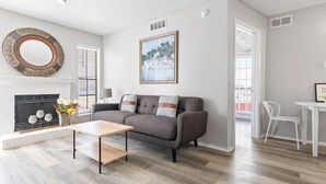 Een moderne woonkamer met een open haard, een grijze bank, een salontafel en een schilderij aan de muur.