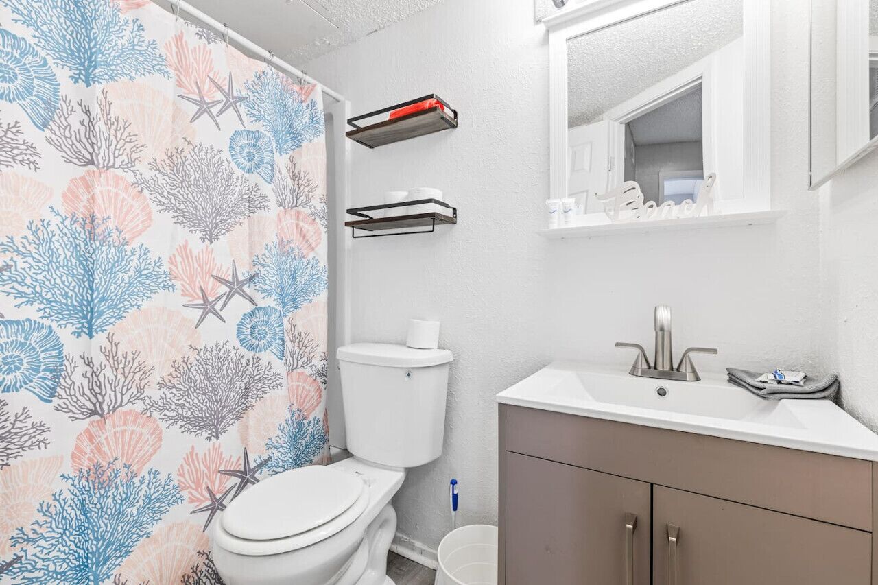 Een badkamer met toilet, wastafel en douchegordijn met een patroon van koraal en zeesterren.