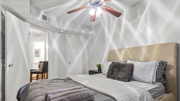 Una camera da letto con un letto, una ventola a soffitto, un comodino e una sedia.