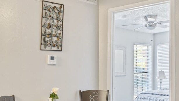 Zona pranzo con tavolo e sedie, ventilatore a soffitto, bocchetta di ventilazione a parete e una porta che dà su un'altra stanza.