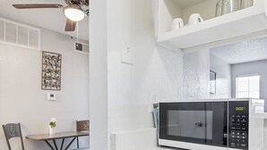 Una cucina compatta con forno a microonde, un piccolo tavolo da pranzo con sedie e una ventola a soffitto.