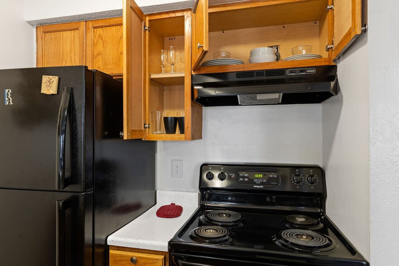 A kitchen with a black refrigerator, a stove, wooden cabinets, and a countertop.