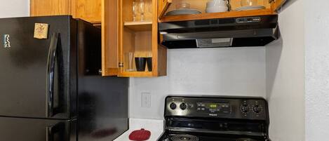 A kitchen with a black refrigerator, a stove, wooden cabinets, and a countertop.