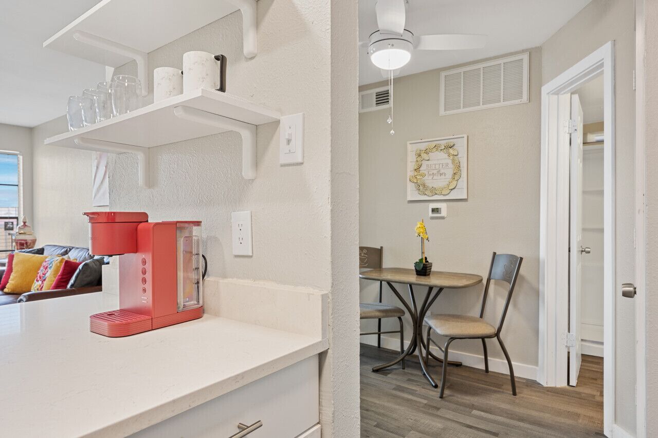 A modern kitchen with white cabinetry, a red coffee machine, and a dining area with a wooden table and chairs.
