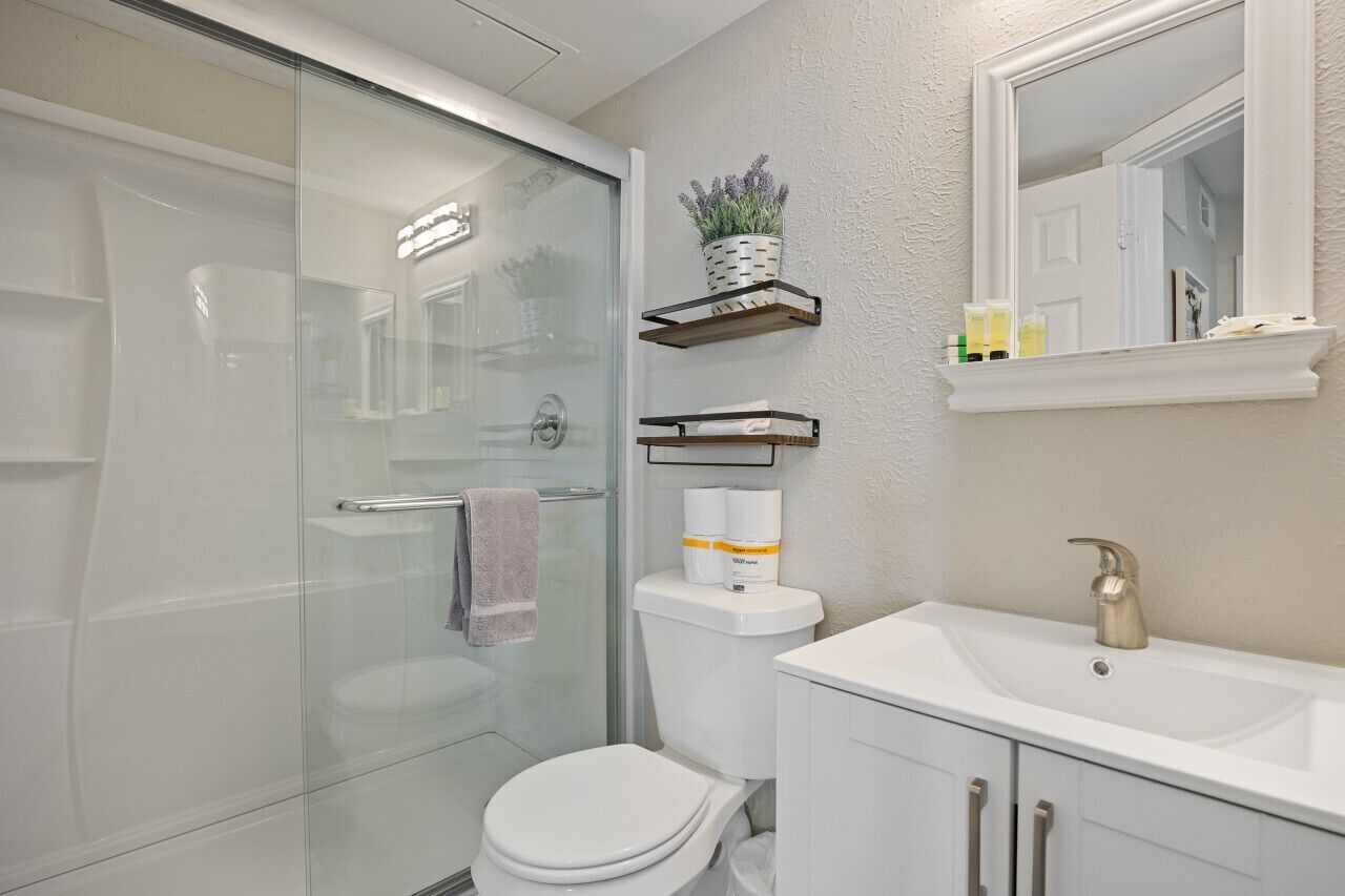 Une salle de bain moderne avec une douche à parois de verre, des toilettes, un lavabo avec un miroir et des étagères contenant des articles de toilette.