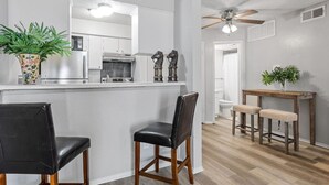 A modern kitchen with white cabinets, a stainless steel refrigerator, and a wooden dining area with two stools. - Simplicity and Convenience! Pool View w. Balcony! (Dallas)