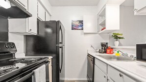 A compact kitchen with a black stove, white cabinets, and a stainless steel refrigerator. - Central DFW 1 Bed Apt! (Dallas)