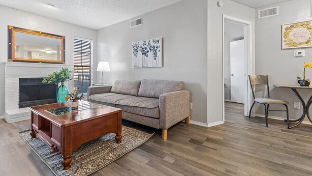 A living room with a fireplace, a sofa, a coffee table, and a dining area with a chair and table. - Central DFW 1 Bed Apt! (Dallas)