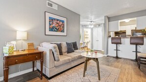 A living room with a sofa, coffee table, and a dining area with bar stools. - COZY CORPORATE UNIT IN DFW! (Dallas)