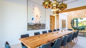 A modern dining area with a long wooden table, blue upholstered chairs, and a large abstract painting on the wall.