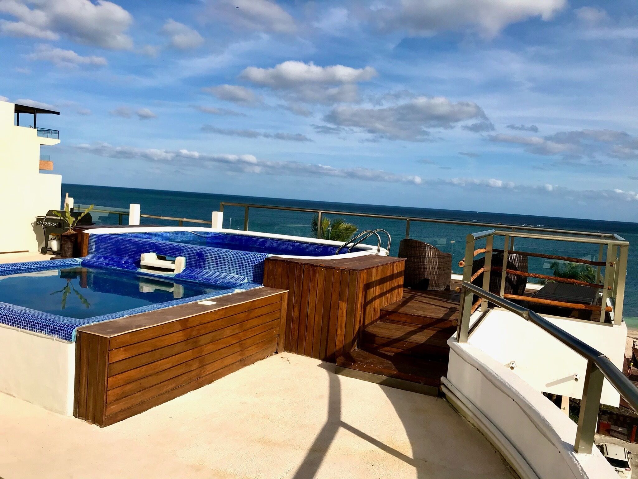 En pool på taket med utsikt över havet, ett trädäck och solstolar.