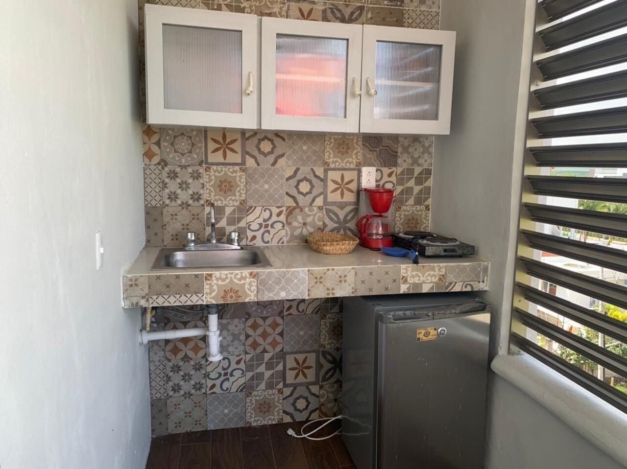 A compact kitchen with patterned tiles, a sink, a coffee maker, and a refrigerator.