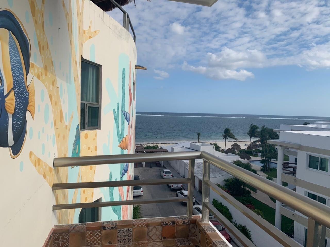 Un balcón con vista al océano y un edificio con un mural colorido.