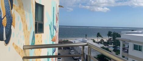 Un balcón con vista al océano y un edificio con un mural colorido.