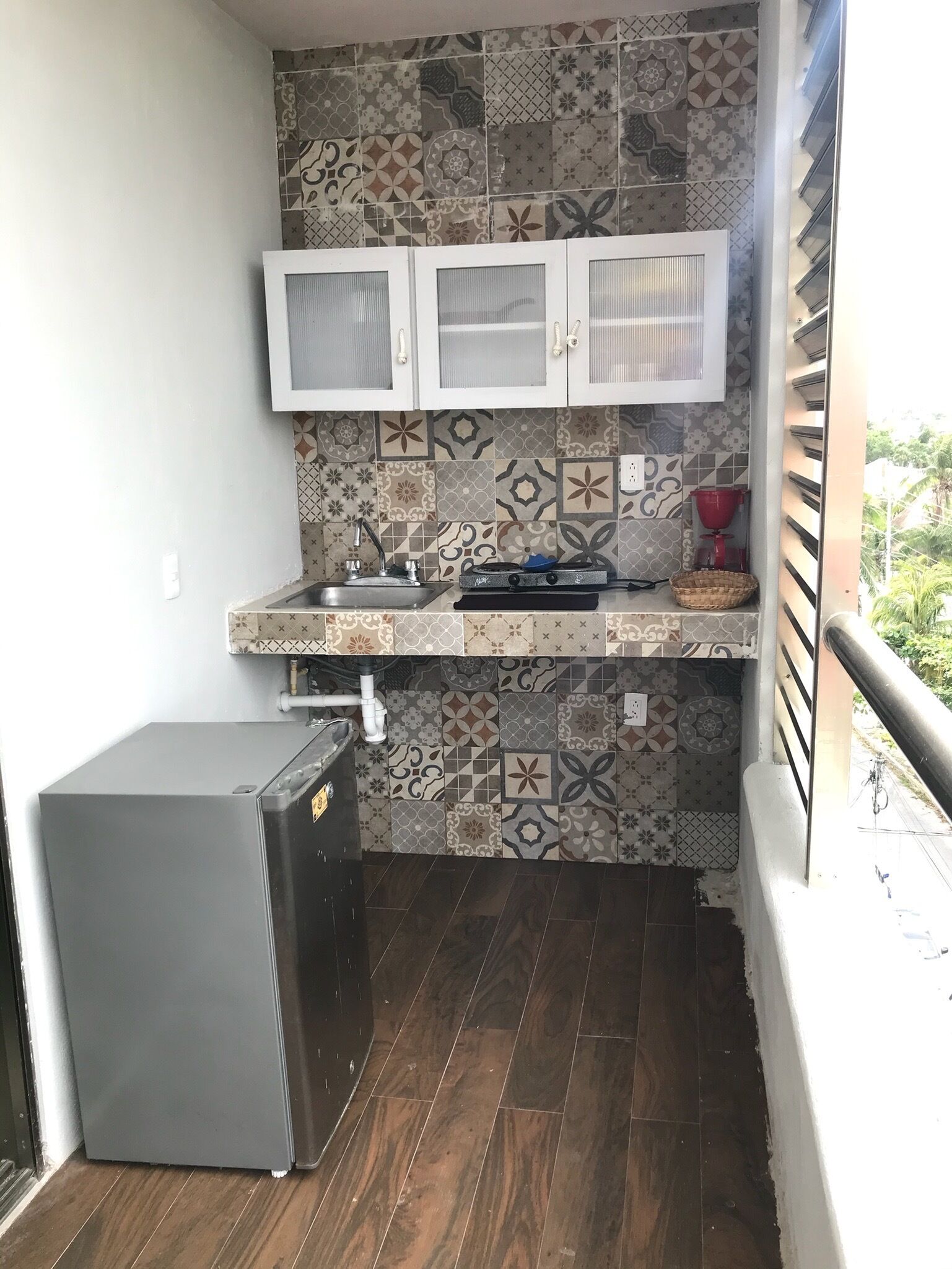 A compact kitchen with patterned tiles, a sink, a stove, and a small refrigerator.