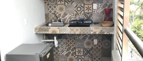 A compact kitchen with patterned tiles, a sink, a stove, and a small refrigerator.