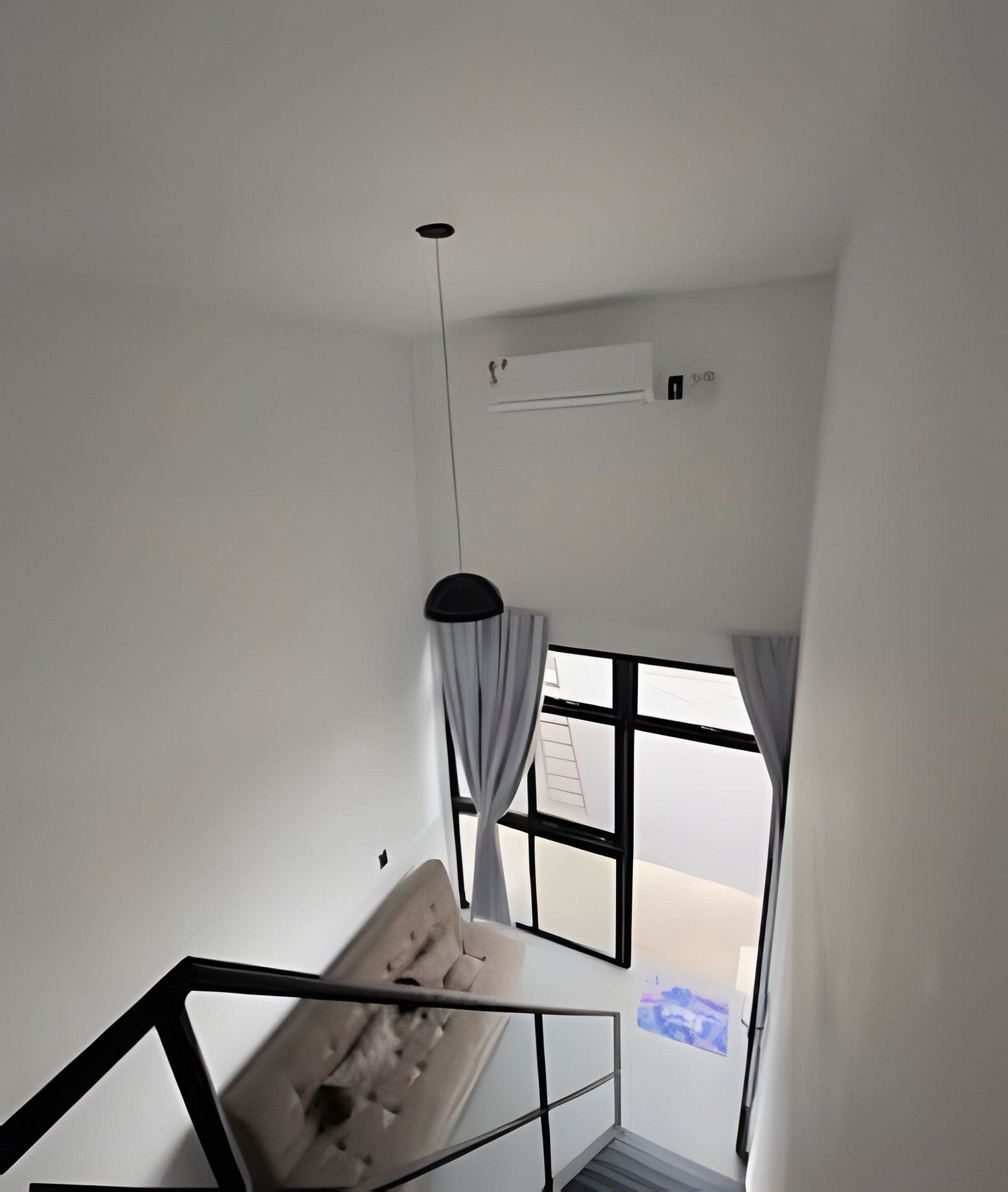 Un interior moderno con una escalera, una lámpara colgante y un ventanal con cortinas.