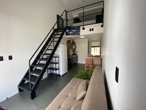 A compact living space with a staircase, kitchenette, and a sofa. - Lofts Meia Morada (São Francisco do Sul)
