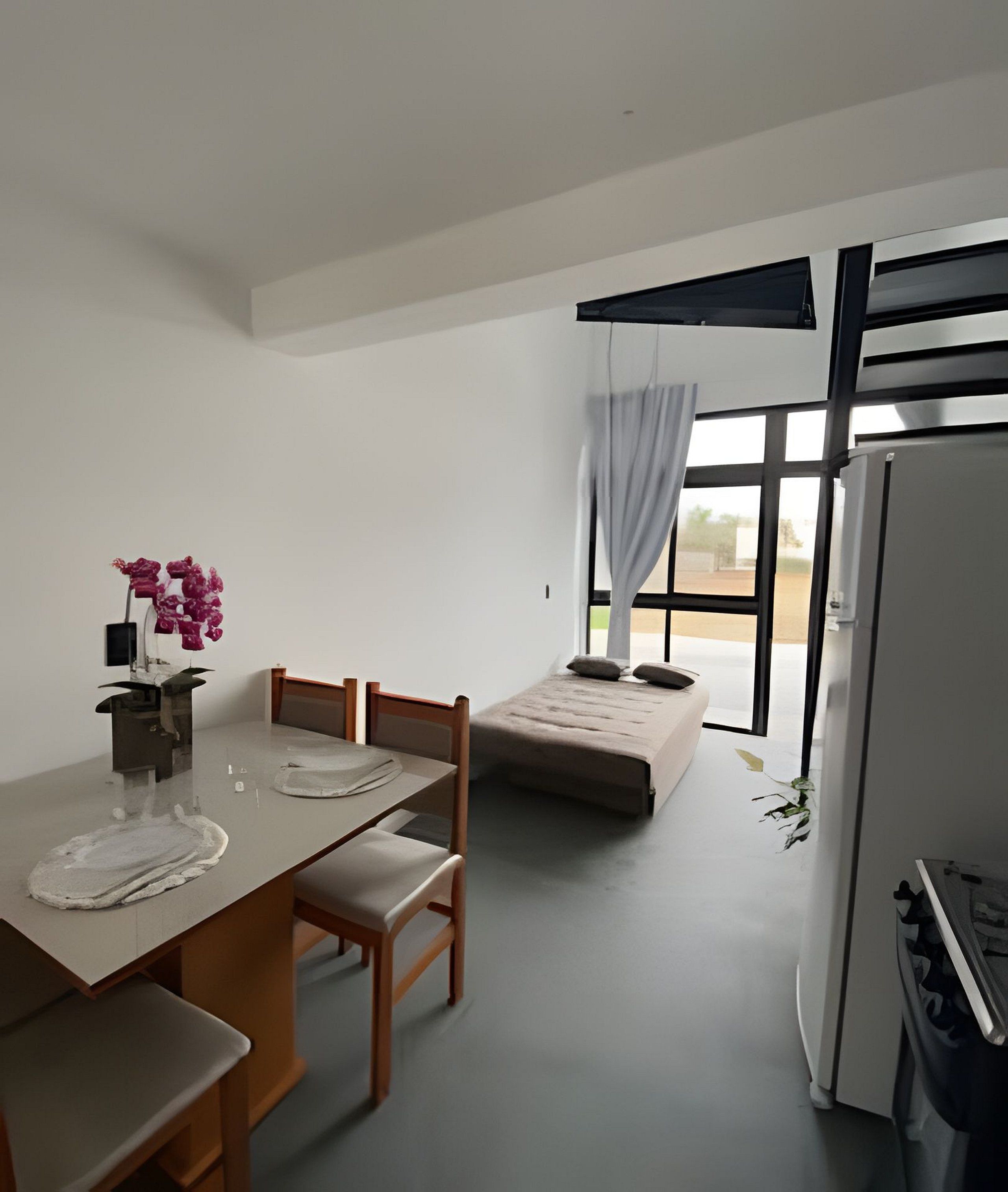 Ein kleiner, moderner Raum mit Esstisch, Stühlen, einer Couch, einem Kühlschrank und einem Fenster mit Vorhängen.