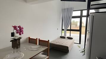 Ein kleiner, moderner Raum mit Esstisch, Stühlen, einer Couch, einem Kühlschrank und einem Fenster mit Vorhängen.