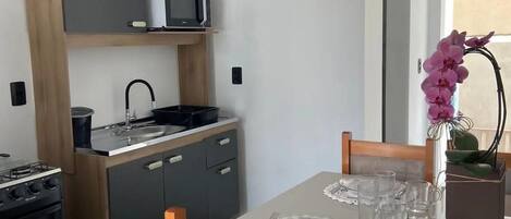 Una cocina moderna con microondas, estufa y lavabo. Hay una mesa de comedor con sillas y un florero con flores.
