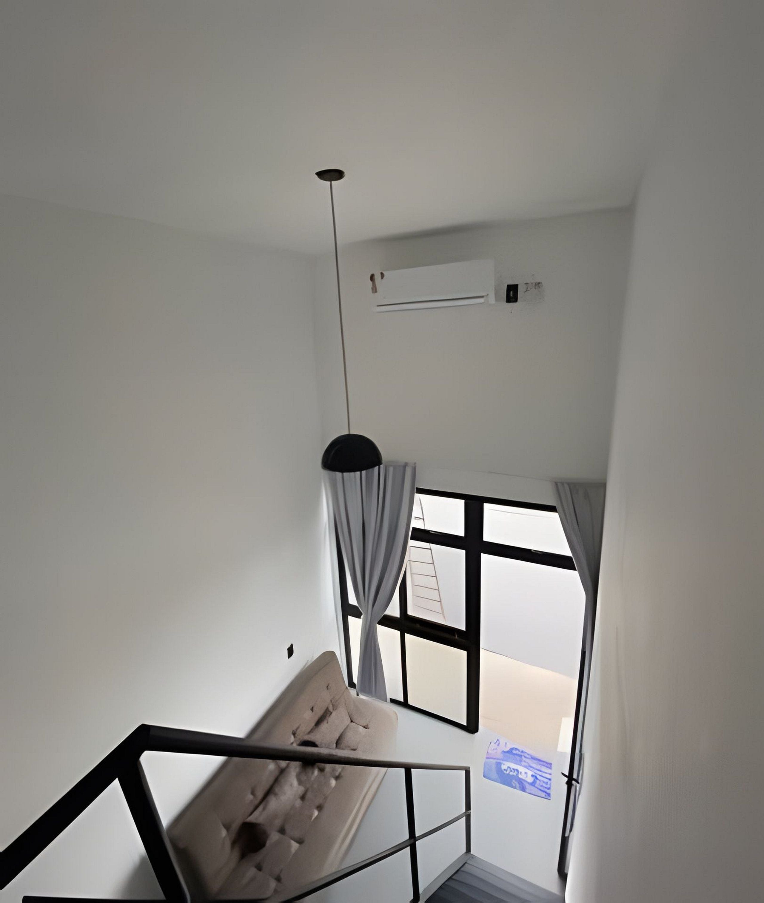 Ein Zimmer mit Bett, einem Vorhangfenster, einer Pendelleuchte und einer Klimaanlage.