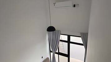 Ein Zimmer mit Bett, einem Vorhangfenster, einer Pendelleuchte und einer Klimaanlage.