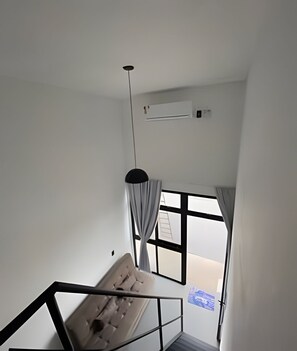 A room with a bed, a window with curtains, a hanging light fixture, and an air conditioning unit. - Lofts Meia Morada (São Francisco do Sul)