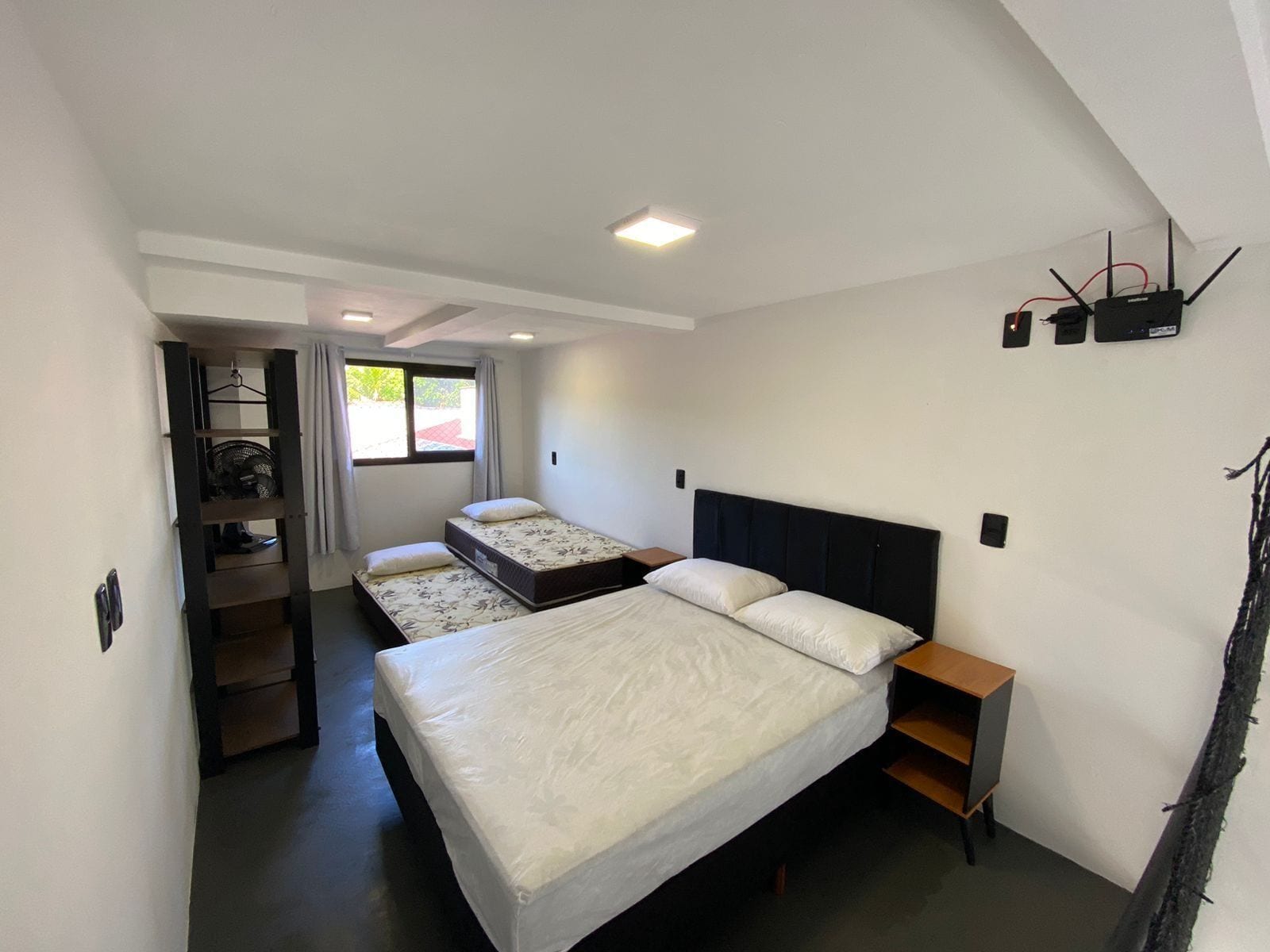 Un dormitorio con dos camas, un escritorio pequeño, una estantería y una ventana.