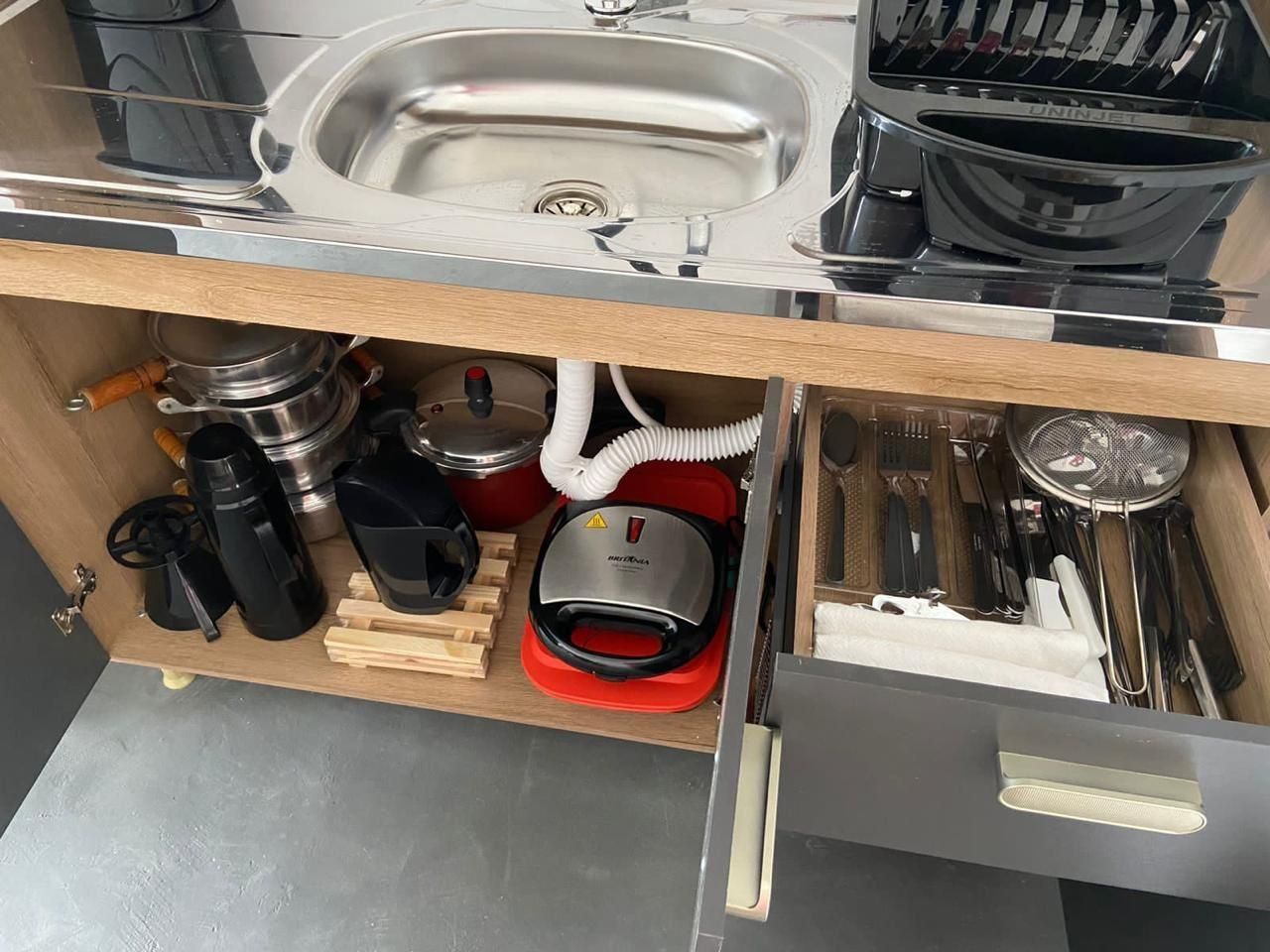 Eine Küche mit einer Edelstahlspüle, einer Kaffeemaschine, einem roten Wasserkocher und verschiedenen Küchenutensilien.