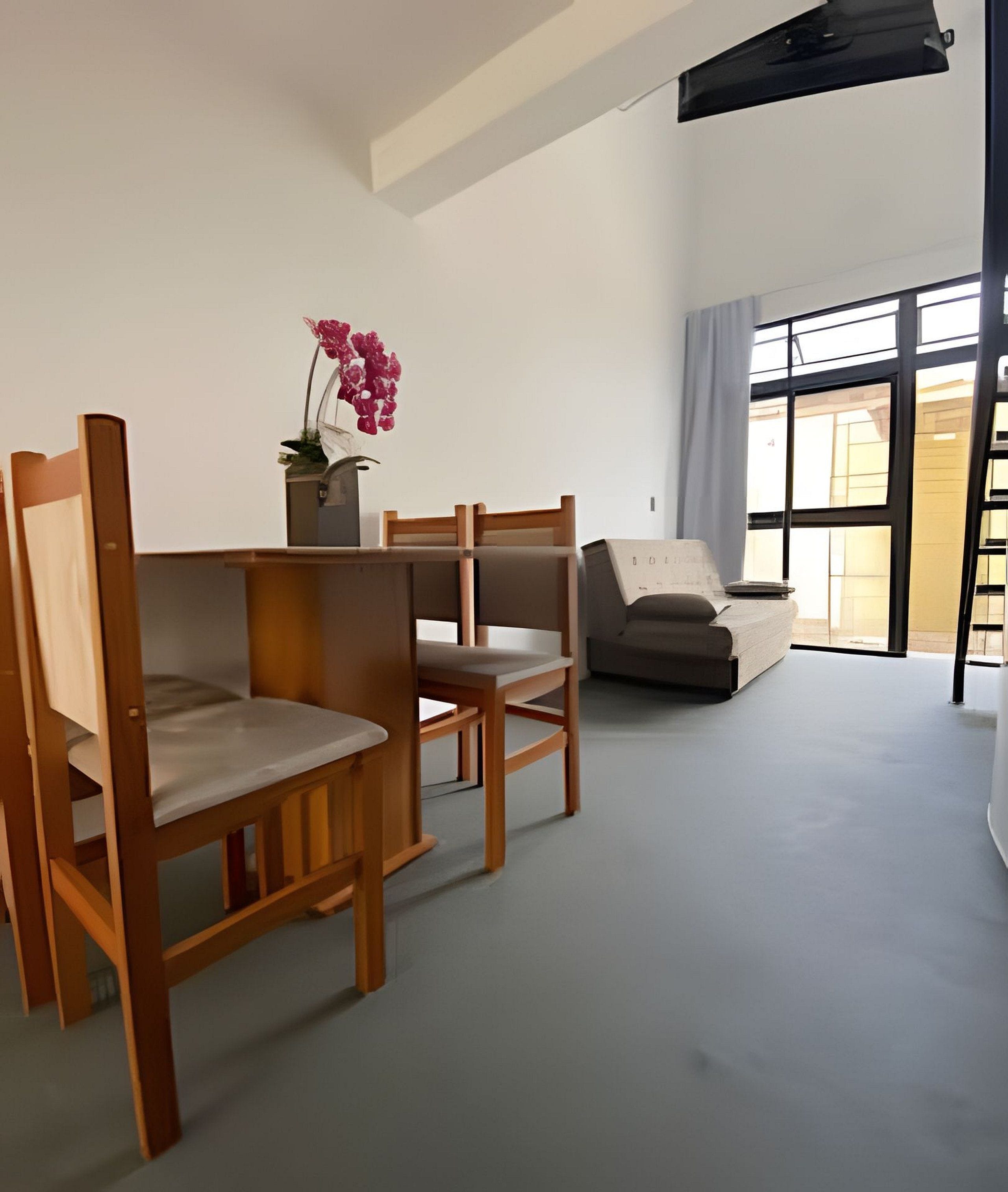 A modern living room with wooden chairs, a sofa, a potted plant, and a large window.