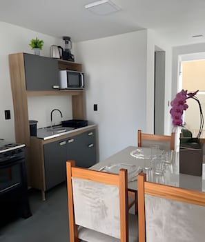 A modern kitchen with a microwave, sink, and cabinets, a dining table with chairs, and a potted plant. - Lofts Meia Morada (São Francisco do Sul)