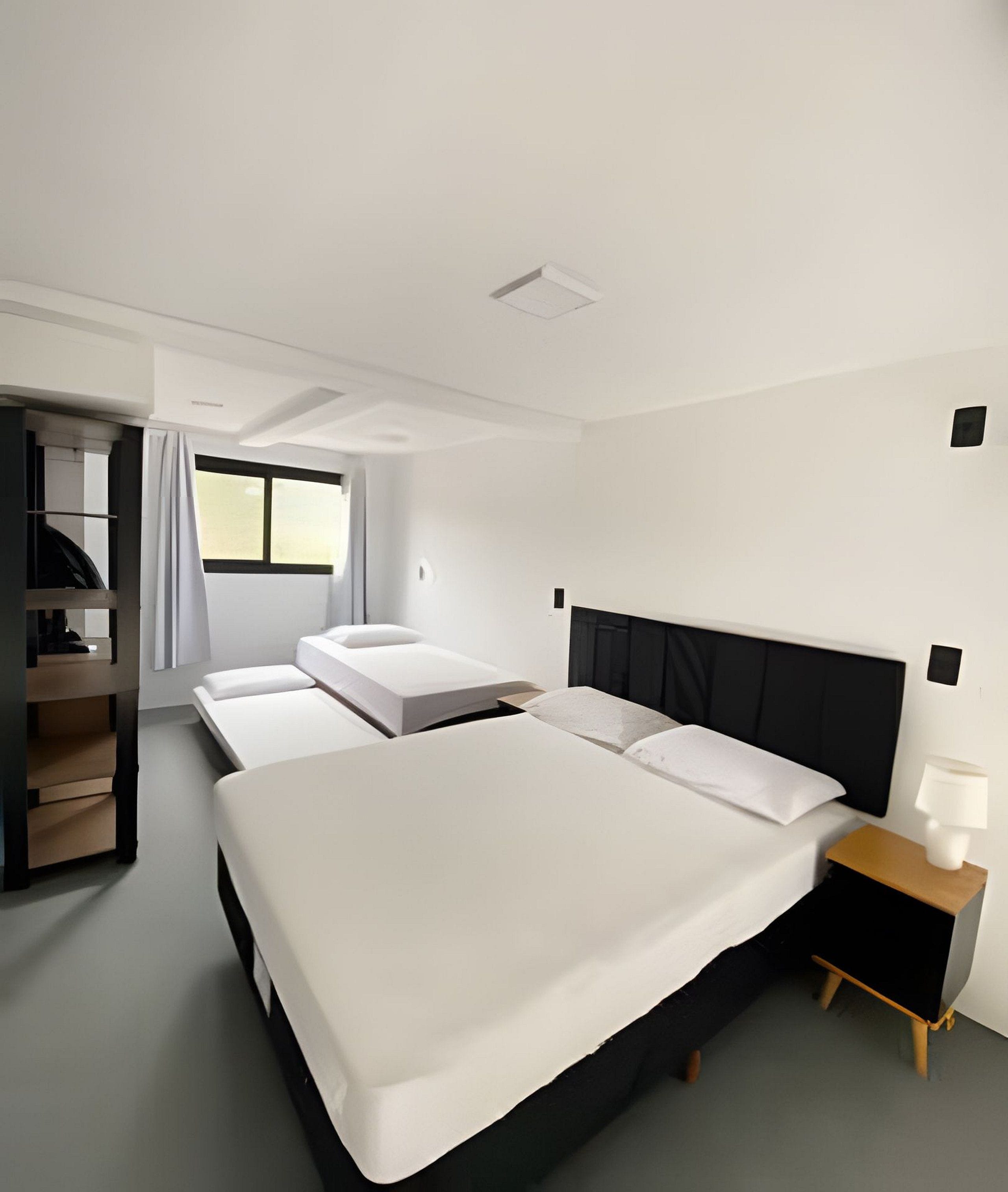 A modern hotel room with a large bed, a smaller bed, a desk, and a wardrobe.