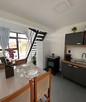 A modern kitchen with a dining area, a staircase, and a view of the outside. - Lofts Meia Morada (São Francisco do Sul)