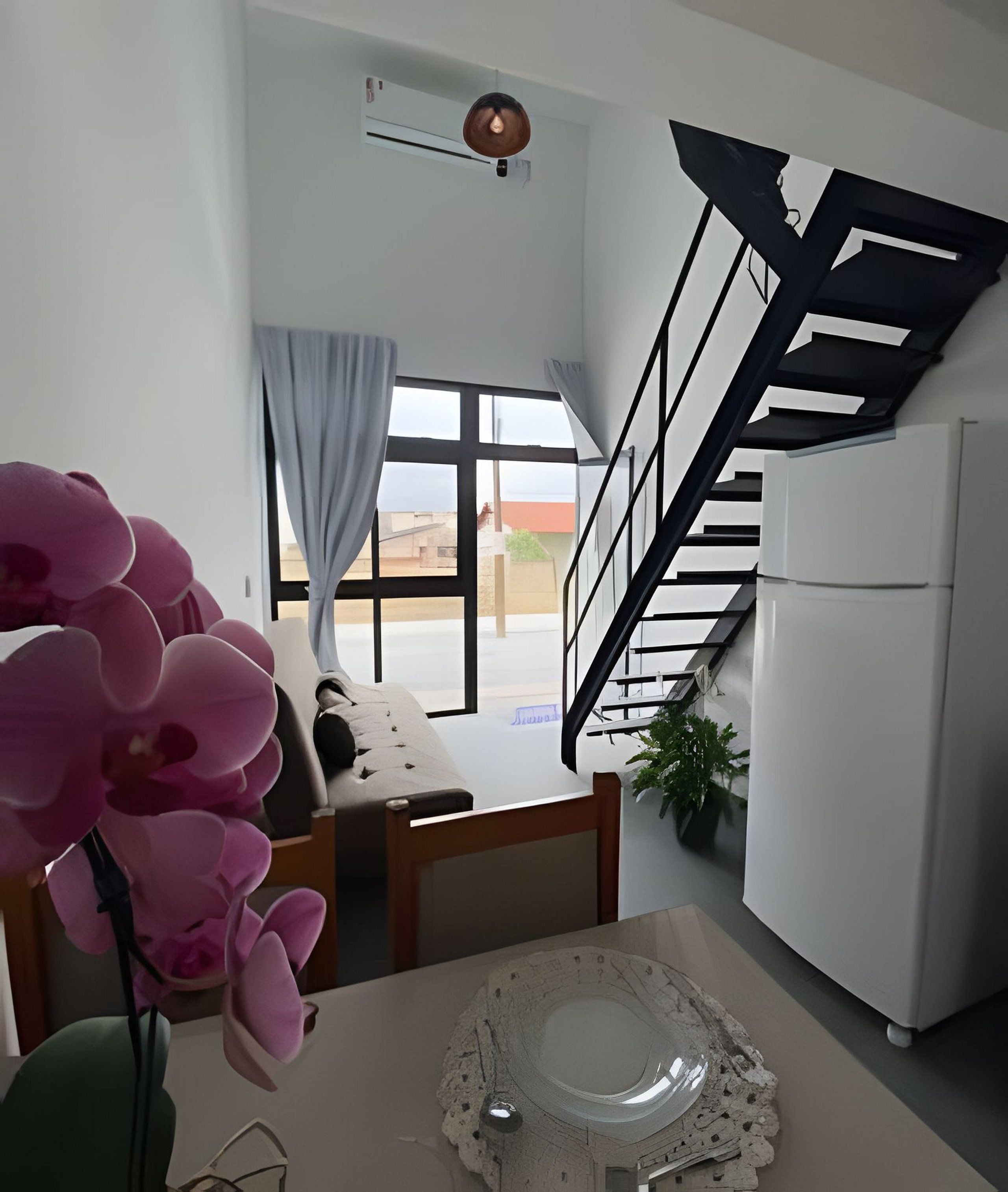 Une cuisine moderne dotée d’un réfrigérateur encastré, un coin repas avec une table et des chaises, un escalier et une grande fenêtre avec des rideaux.