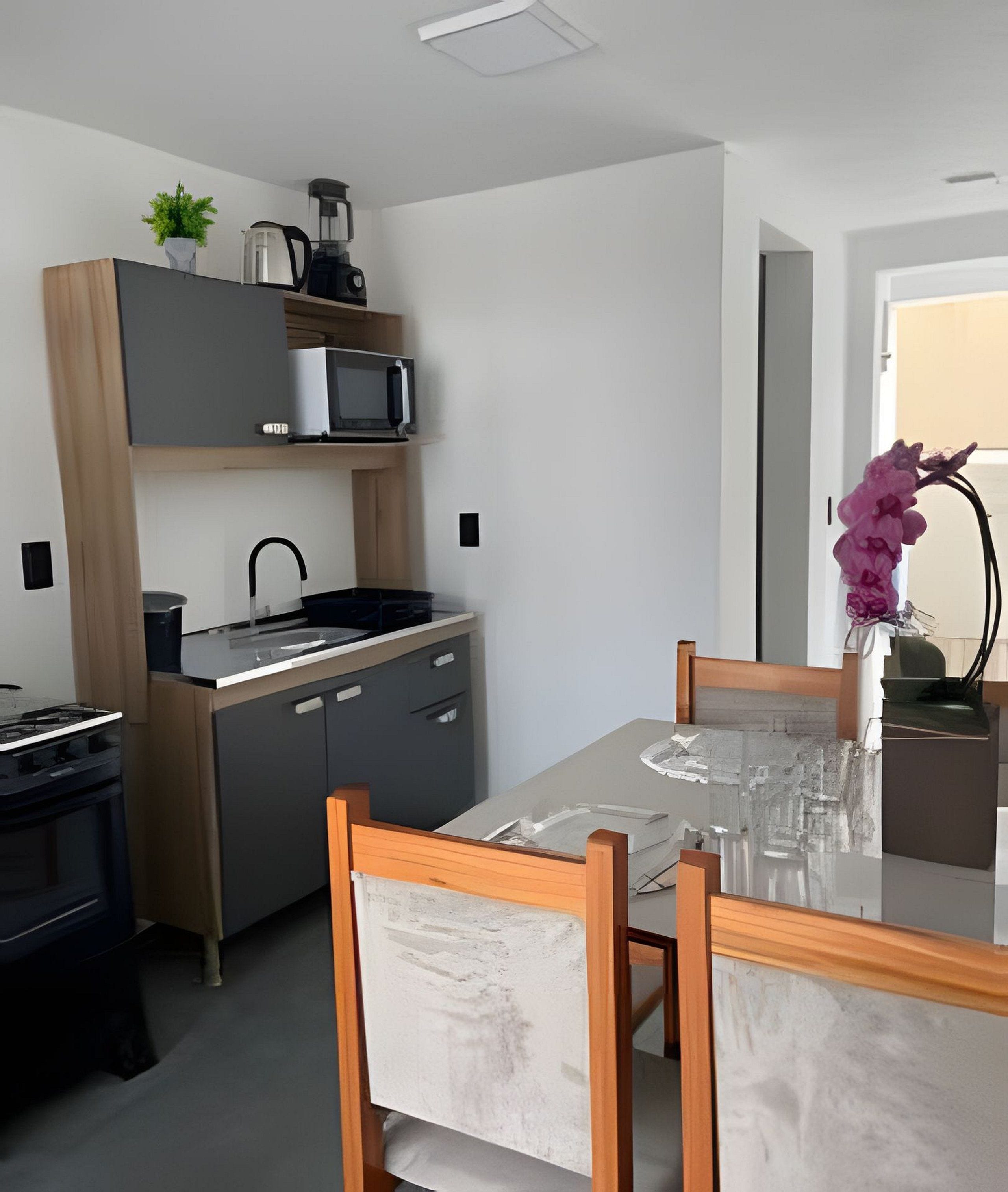 Een moderne keuken met een magnetron, waterkoker en spoelbak. Er is een eettafel met stoelen en een vaas met bloemen.