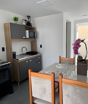 A modern kitchen with a microwave, kettle, and sink. There is a dining table with chairs and a vase with flowers.