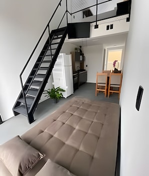 A compact living space with a bed, kitchenette, dining area, and a staircase.