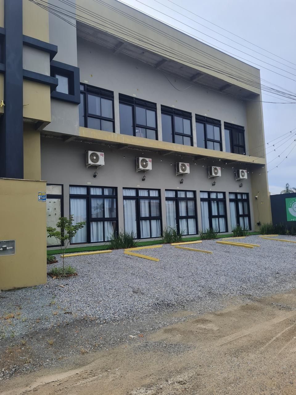 Ein mehrstöckiges Gebäude mit Klimaanlagen, einem Parkplatz mit gelben Markierungen und einem Kiesgrundstück.
