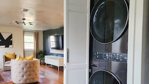 A modern living room with a large, open door leading to a laundry room with two washing machines. - Chic, Spacious Pet Friendly Apt Near Attractions/Food/EWR/NYC (West Orange)