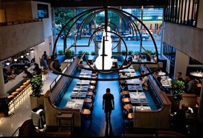 En modern restaurang med en central, cirkelformad design, flera matbord och utsikt över gatan utanför.