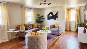 A living room with a brown leather sofa, a grey ottoman, a small white side table, and a large abstract painting on the wall. - Chic, Spacious Pet Friendly Apt Near Attractions/Food/EWR/NYC (West Orange)