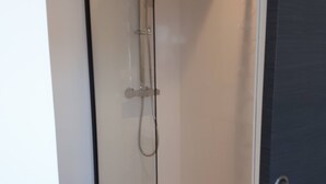 Une douche fermée par des parois en verre, équipée d’un pommeau de douche à main et d’un pommeau de douche fixe.