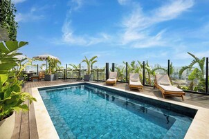 Une piscine sur le toit, avec une eau d’un bleu cristallin, entourée d’une terrasse en bois et de chaises longues.