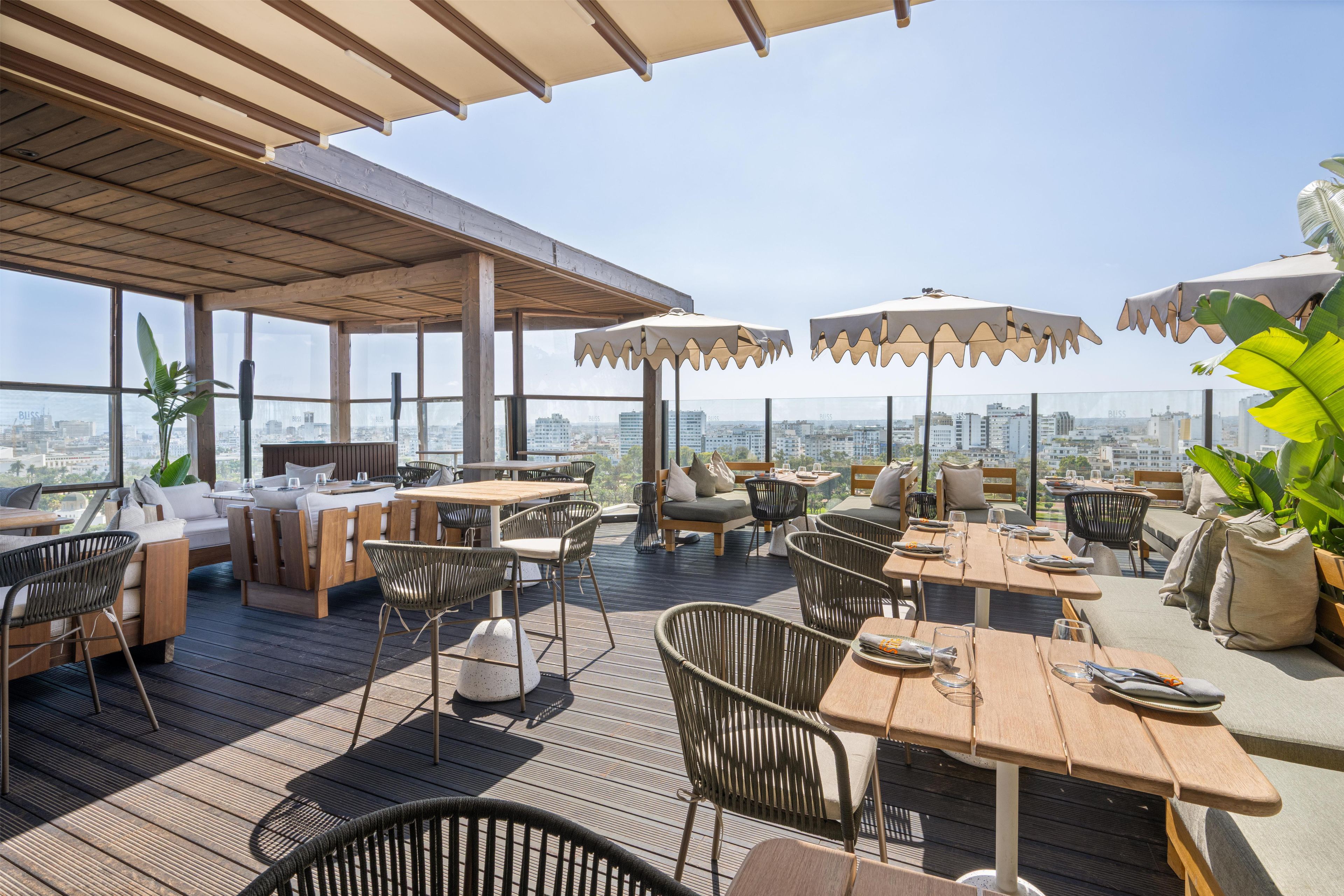 An outdoor terrace with wooden furniture, umbrellas, and a view of the cityscape.