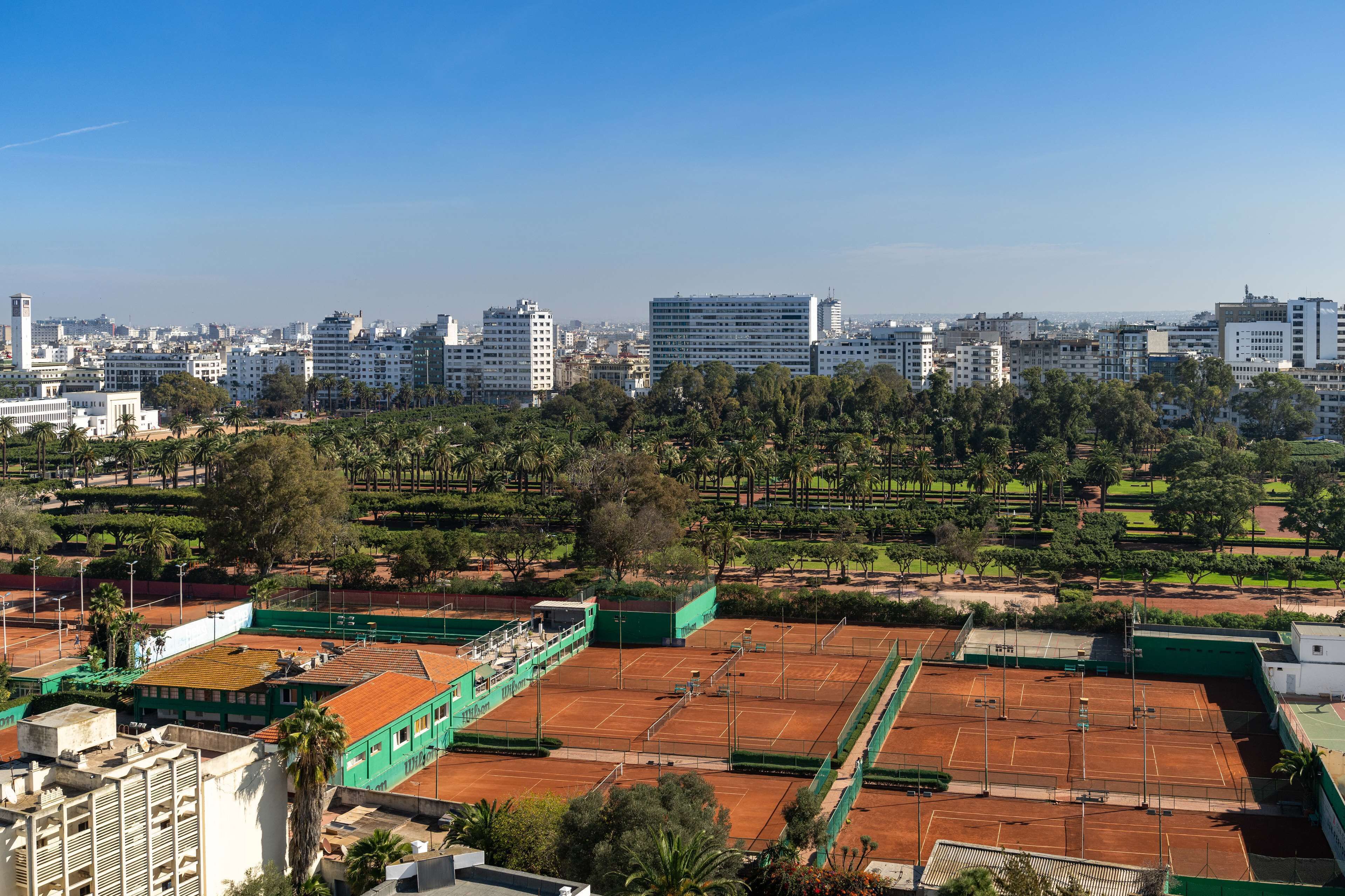 A tennis court surrounded by buildings and greenery.