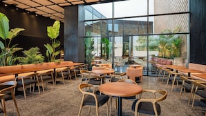 A modern cafe with wooden tables and chairs, large windows, and indoor plants. - Radisson Hotel Casablanca Gauthier La Citadelle (Casablanca)